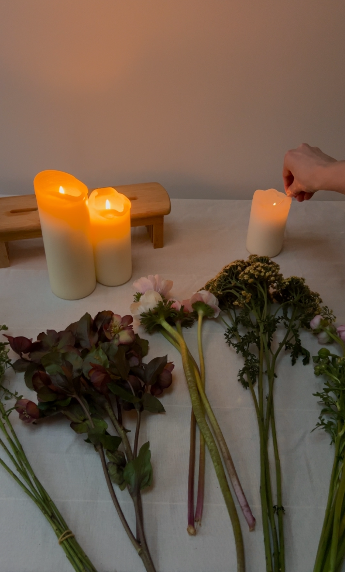 Candles and flowers on a table with a hand lighting one of the candles.